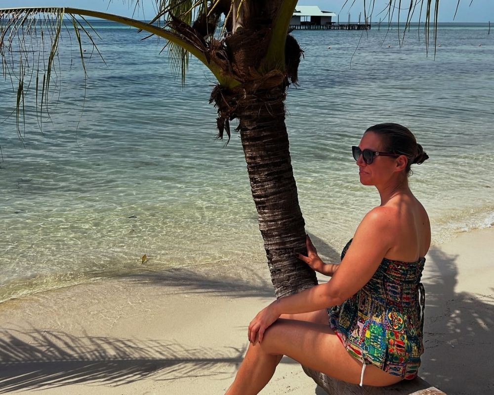 Woman-sitting-under-a-palm-tree-looking-out-to-sea