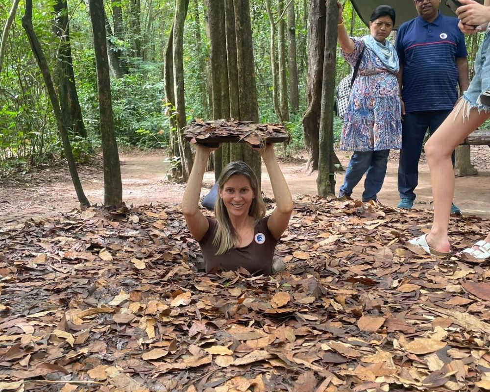 A woman exiting a hidden tunnel entrance covered with leaves at Cu Chi Tunnels